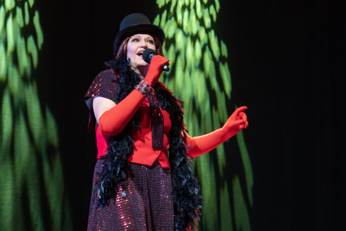 Nainen laulaa silinteri päässään ja punainen mekko yllään